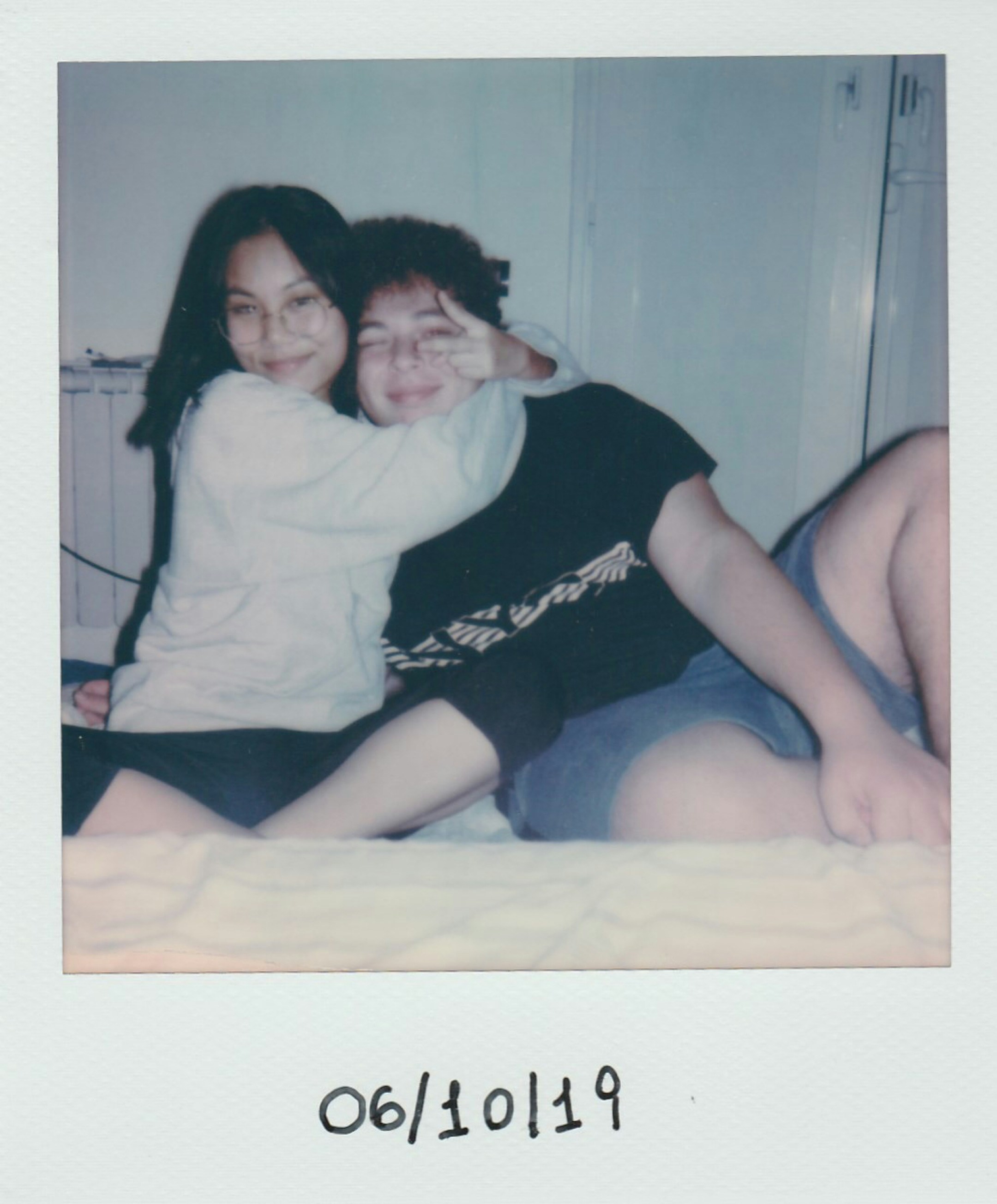Polaroid photo of a couple posing together on a bed with the date 06/10/19 written on the polaroid.